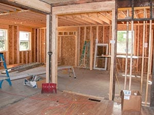 Interior of a home under construction with exposed wooden framing, ladders, and scattered tools on the floor.