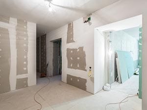 Interior of a building under renovation with partially installed drywall and taped seams, and exposed wiring on the floor.